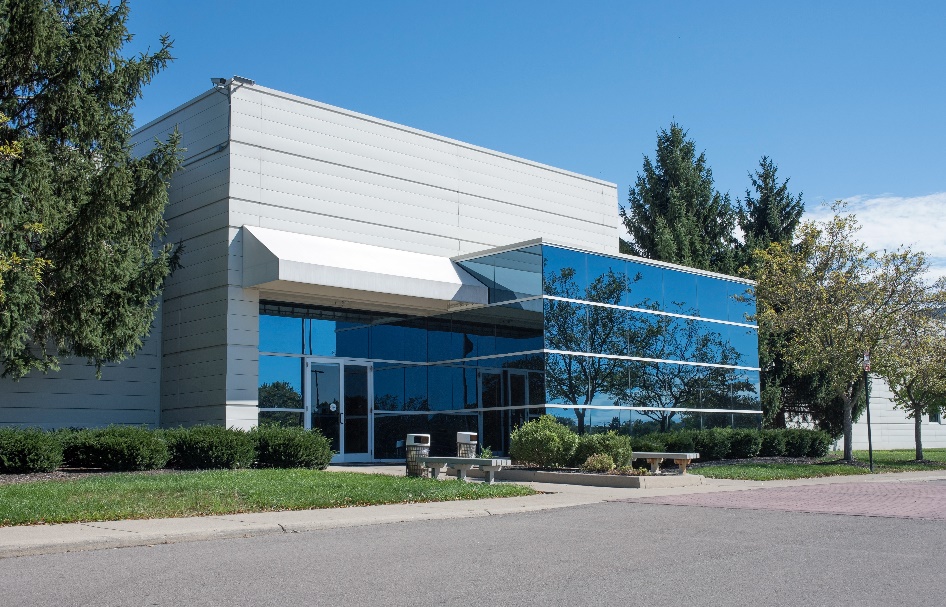 A commercial building with very tinted glass reflecting trees and sunlight.